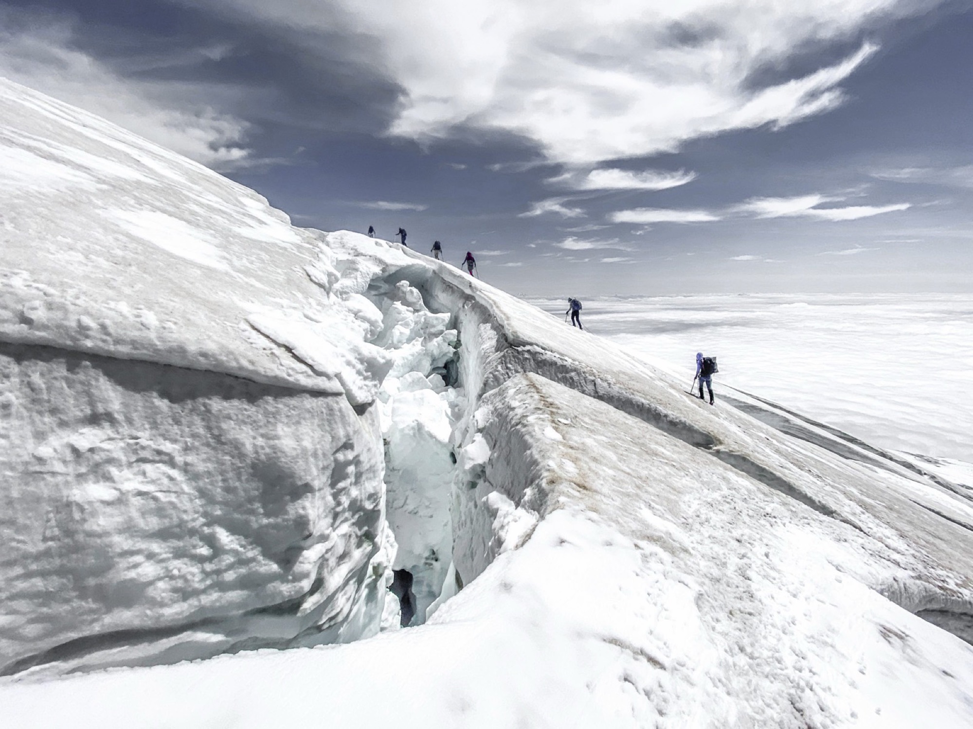 A rope team crossing a glacier past an open crevasse on Mount Baker